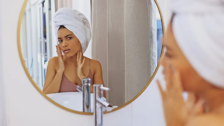 Shot of an attractive young woman inspecting her face in the bathroom mirror