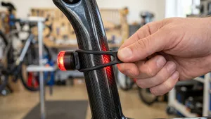 Close-up van een hand die een led-achterlicht met een strak rubberen bandje om de carbon zadelpen van een racefiets monteert.
