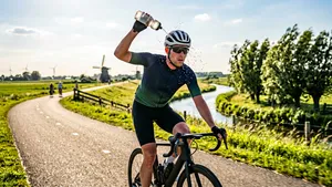Mannelijke wielrenner op de fiets die op het punt staat een bidon met water over zijn helm te knijpen op een hete zomerdag.