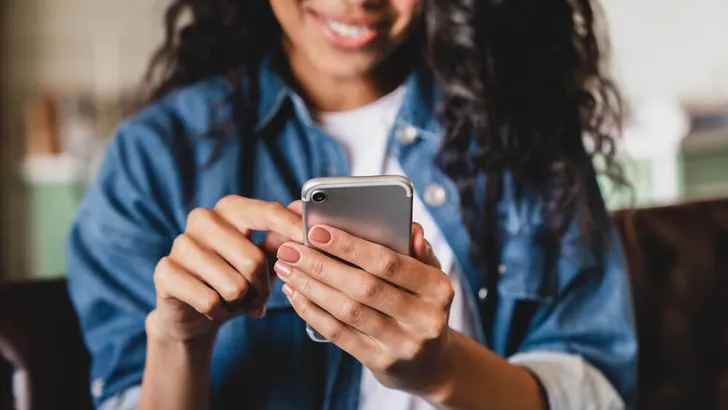 Cropped shot of an african-american young woman using smart phone at home. Smiling african american woman using smartphone at home, messaging or browsing social networks while relaxing on couch