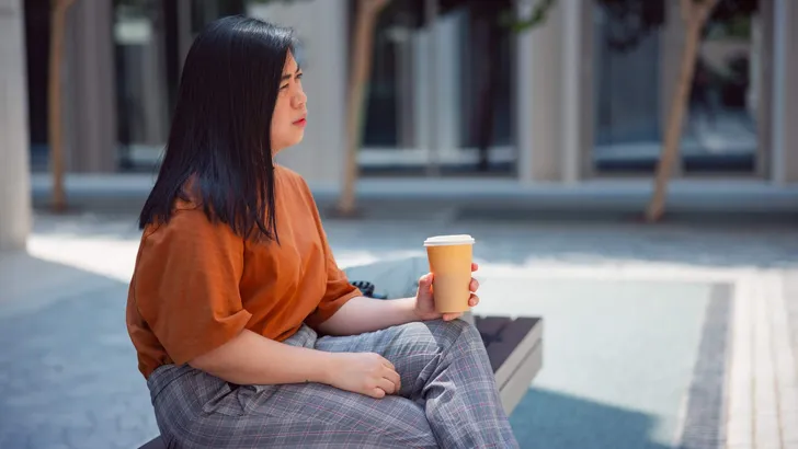 Woman holding her reusable cup and sitting on a street bench