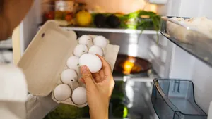 Vrouwenhand haalt doosje eieren uit een koelkast om een gekookt ei te bewaren.