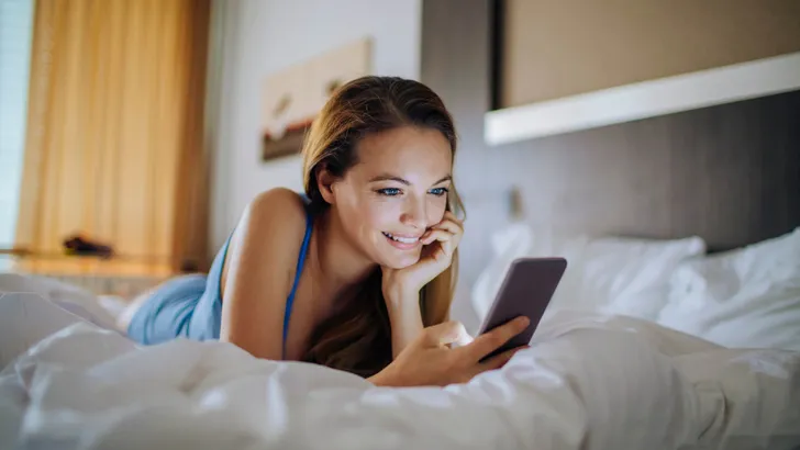 Photo of a young woman laying in bed using smartphone
