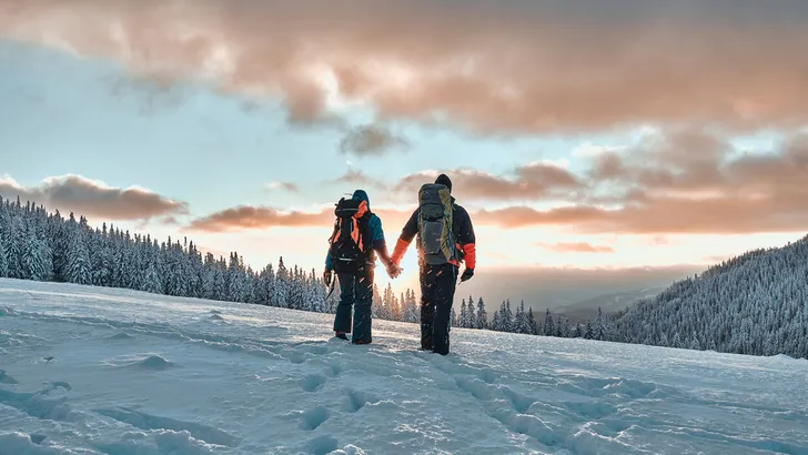 Rest in the mountains. Family couple holding hands and walking in the snowy pine mountains at sunset. The concept of recreation and tourism in winter.