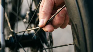 Gedetailleerde macrofoto van een hand die de spaakspanning controleert door twee spaken van een racefietswiel samen te knijpen, met een onscherpe achtergrond.
