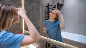 Een verzorgde vrouw van 50+ reinigt haar gezicht aan de wastafel met lauw water, in plaats van het gezicht te wassen onder de douche.