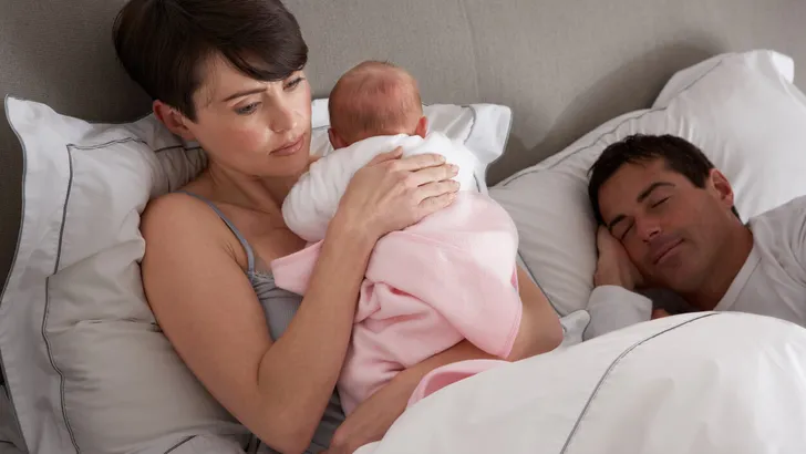 Mother Cuddling Newborn Baby In Bed At Home