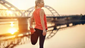 Cute Caucasian blonde woman in sportswear stretching leg by the river. It's hard to beat a person who never gives up.