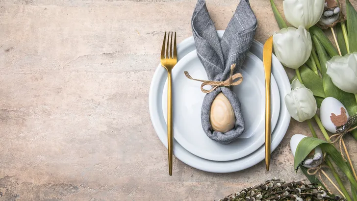 Gedekte paastafel met een paashaasje van een ei op een wit bord en tulpen. Grijze betonnen tafel, bovenaanzicht met ruimte voor tekst. Vrolijk Pasen achtergrond