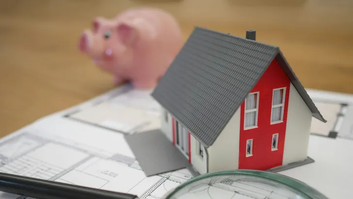 Beleggen in vastgoed. – Foto van miniatuur-huisje op plattegrond bij spaarvarken.