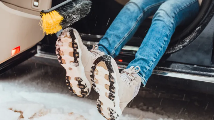 Persoon veegt besneeuwde schoenen schoon voor instappen in de auto.