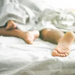 Close up of male and female feet on a bed - Loving couple having sex under under white blanket in the bedroom - Concept of sensual and intimate moment of lovers - Vintage filter - Focus on male foot