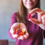 Closeup image of a young woman holding and showing at a red jelly gummy bears