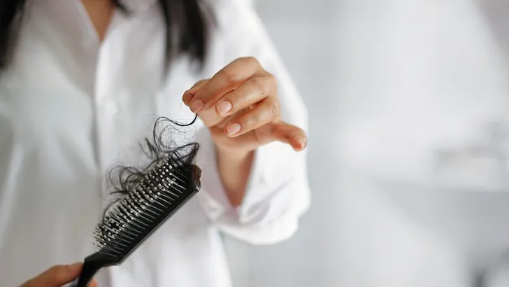 woman losing hair on hairbrush in hand on bathroom background