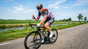 Een hevig zwetende wielrenner fietst in de brandende zon en steekt ondanks de hitte positief zijn duim op naar de camera.