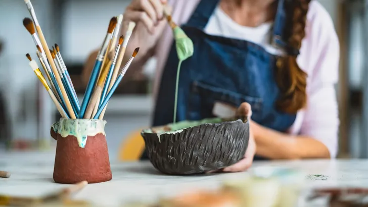 Woman mixing paint with brush inside ceramic bowl in workshop studio - Artisan work and creative craft concept