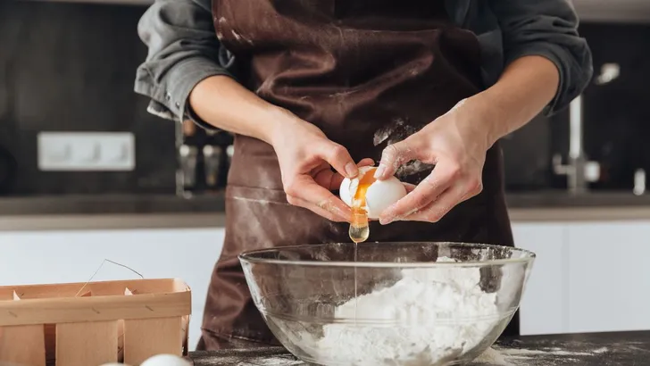 Een vrouw in de keuken die een ei aan de bakmeel toevoegt