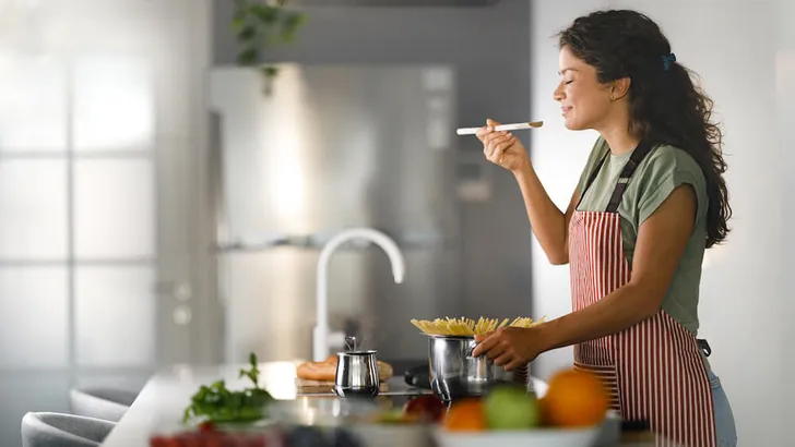 Smiling woman enjoying while cooking spaghetti for lunch.