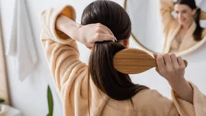 back view of young brunette woman brushing hair in bathroom.