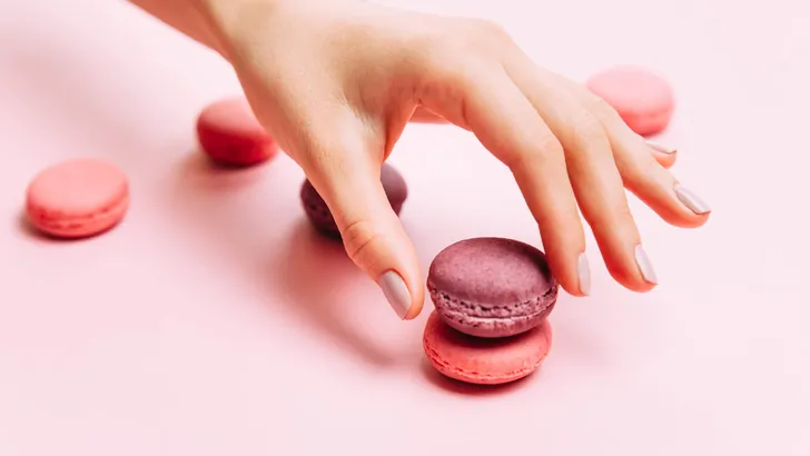 Beautiful female hands with trendy manicure holding pink macaroon cake.