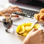 Girl works at a computer and eats fast food. Unhealthy food: chips, crackers, candy, waffles, cola. Junk food, concept.