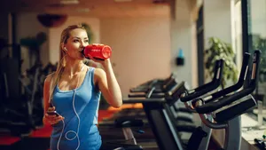 Beautiful young woman resting and drinking water in the gym