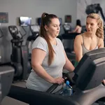 Caucasian instructor helping plus size woman at the gym