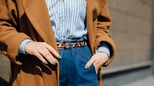 Close-up streetstyle-foto van model met lichte blouse, jeans, panterprint-riem en een cognacbruine jas.