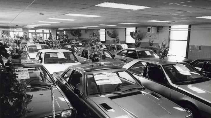 In de showroom van een autodealer staan rijen auto's te koop, elk met de prijs op de voorruit geplakt, Nederland 1989.