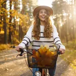 Happy active woman in stylish clothes rides a bicycle in an autumn park at sunset. Outdoor portrait. Beautiful woman enjoying nature. Active lifestyle.