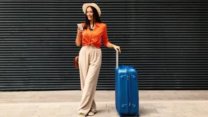 Vrouw in vakantiekleding poseert voor zwarte muur met blauwe koffer.