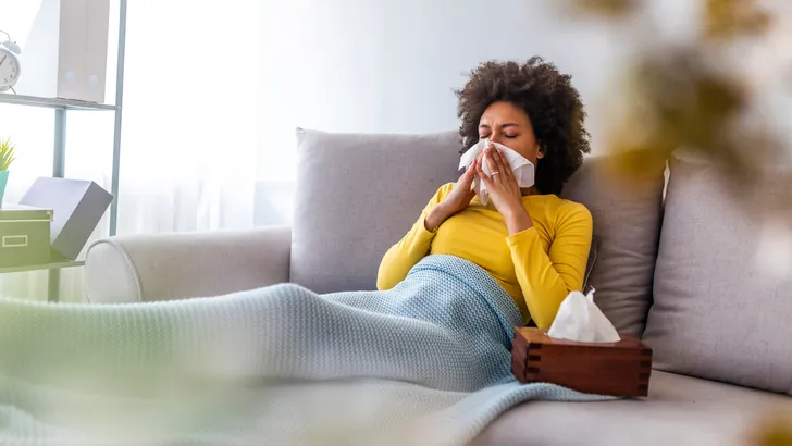 Woman blowing her nose on couch at home in the living room.