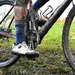 Close-up van een mountainbiker met modderige benen en fiets op een nat grasveld, de wielen en het frame bedekt met dikke blubber na een zware rit.