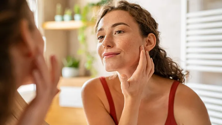 Young beauty woman checking her skin at mirror in the morning