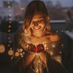 Young, smiling woman standing outdoors on the decorated terrace of her apartment and holding string lights