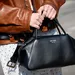 Close-up van vrouw die bruin leren jasje draagt, witte stippen rok en zwarte prada tas - kleurencombinaties zomer