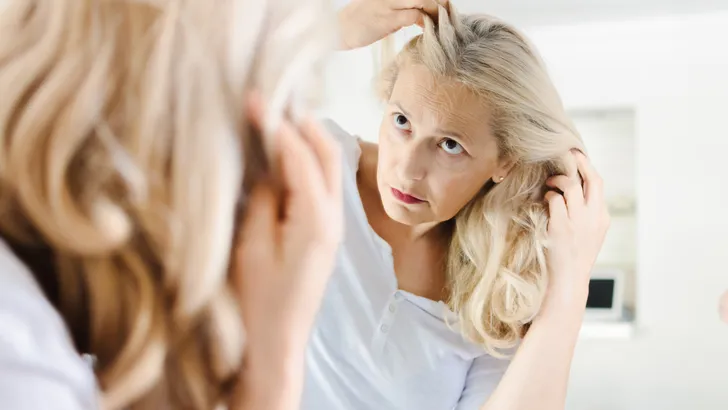 Vrouw kijkt in de spiegel op zoek naar grijs haar.