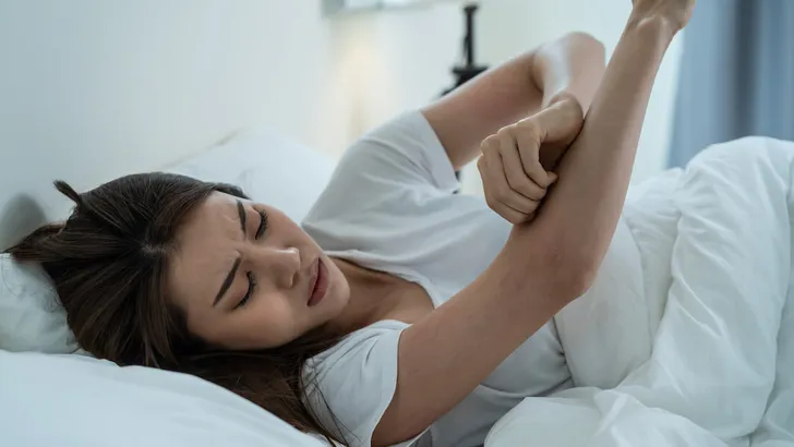 Asian young woman scratch hand feel suffer from allergy while sleeping. Beautiful attractive girl lying on bed in bedroom suffering from itching arm skin allergic reaction to insect bites, dermatitis.