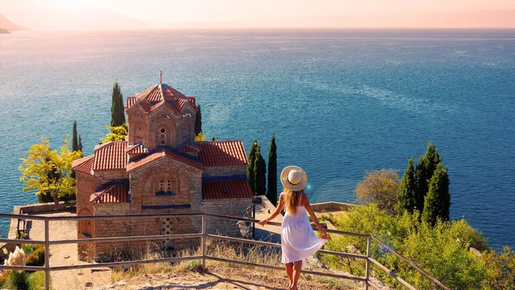 Young female in white dress and hat enjoying panoramic view of famous church,  Ohrid lake in Macedonia