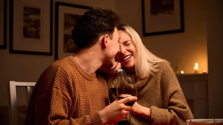 Happy young couple hugging laughing drinking wine on Valentines day at home.