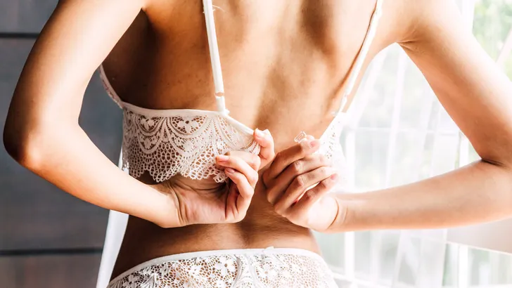 Young sexy woman in underwear unhooking and taking off on her white bra in the room