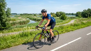 Een vitale mannelijke wielrenner met fietshelm fietst vol energie door een groen Nederlands natuurgebied.
