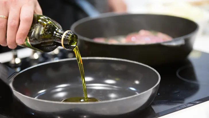 vrouw doet extra vierge olijfolie in pan
