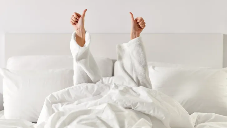 hands of woman lying in bed and showing thumbs up