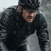 Wielrenner op een racefiets in zware regen, donker regenjack is verzadigd met water, druppels op rits en bril, intense racehouding.