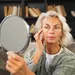 Vrouw smeert selftan op haar gezicht en kijkt in de spiegel.
