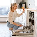 Smiling young white woman putting dishes in the dishwasher at home