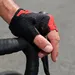 Close-up van een hand in een zwarte, te strakke fietshandschoen die een racefietsstuur vastklemt, waardoor de stof spant en drukpunten op de handpalm zichtbaar worden.
