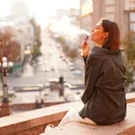 Woman at sunset with amazing city view, enjoying warm days, freedom, positive vibes, smoking  electronic cigarette