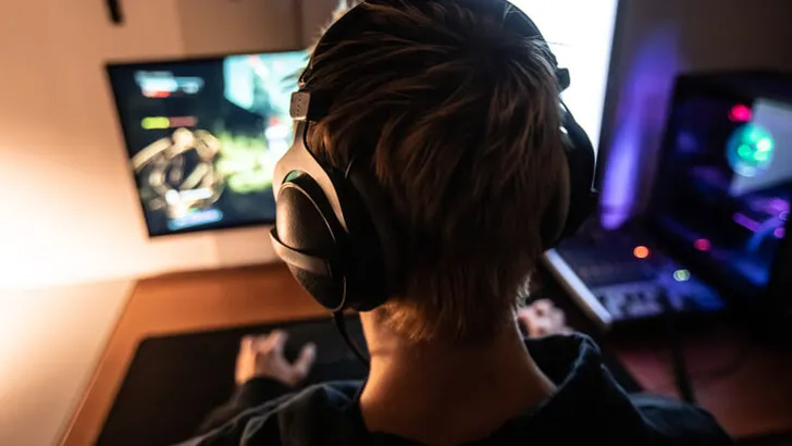 Rear View of Gamer with Headset on Playing Online Video Games in Dark Room - stock photo